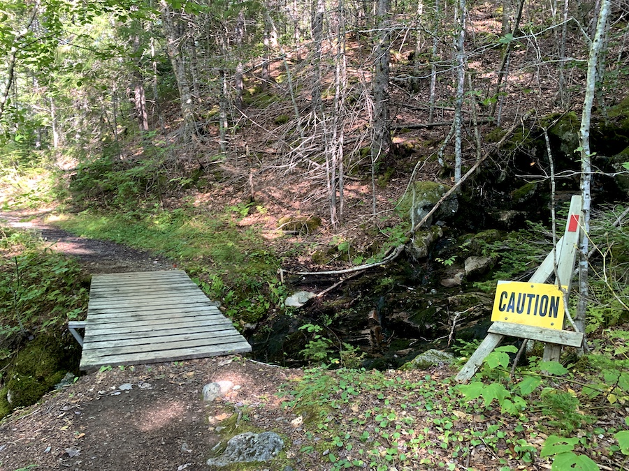 A wooden bridge on the trail to cross a small river with a caution sign. 