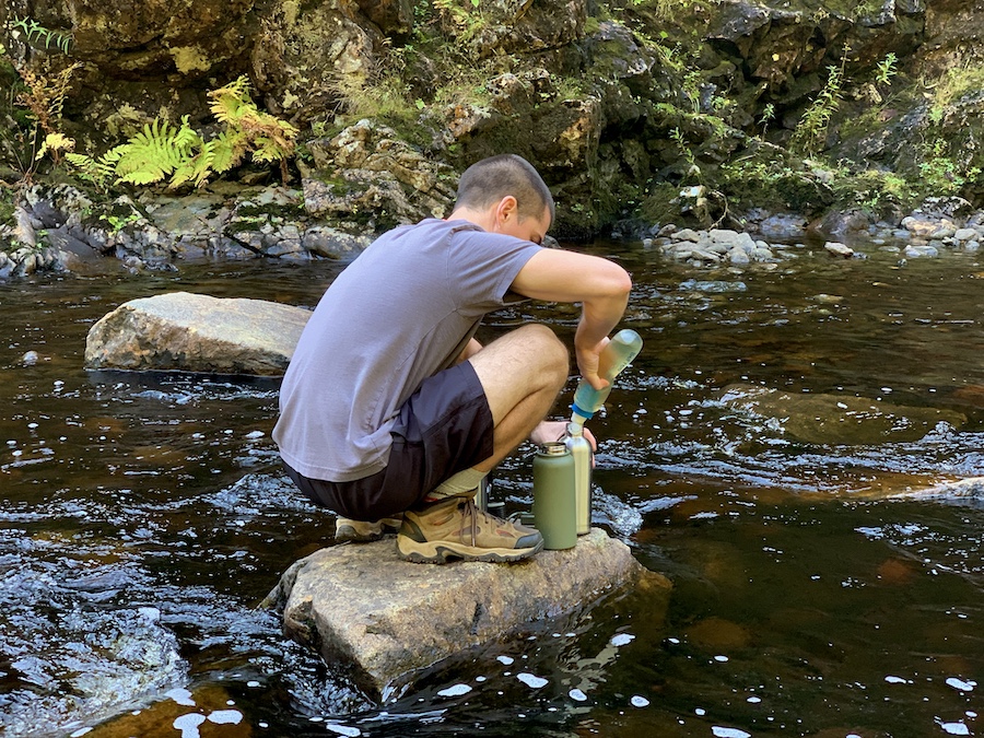 Arthur filling up our water bottles in the river using a Katadyn Befree water filter. 