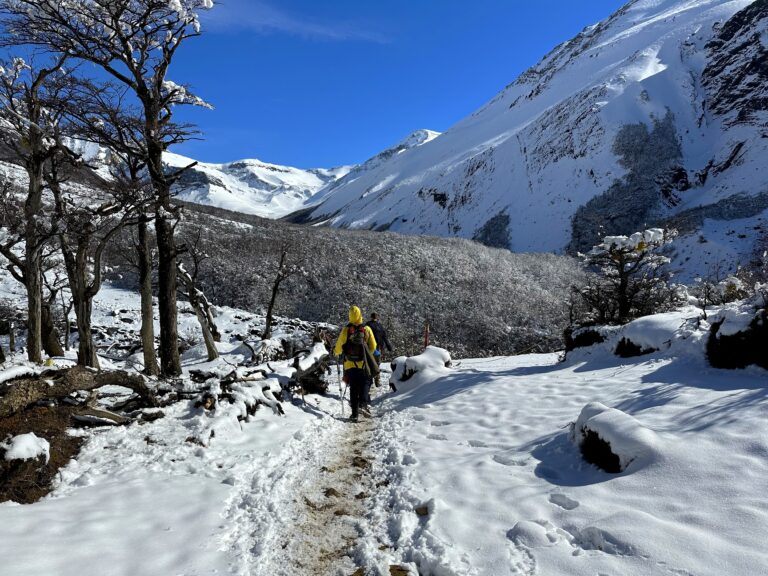 A hiker wearing a yellow jacket on a snowy trail in Patagonia with the snow covered mountains in the background